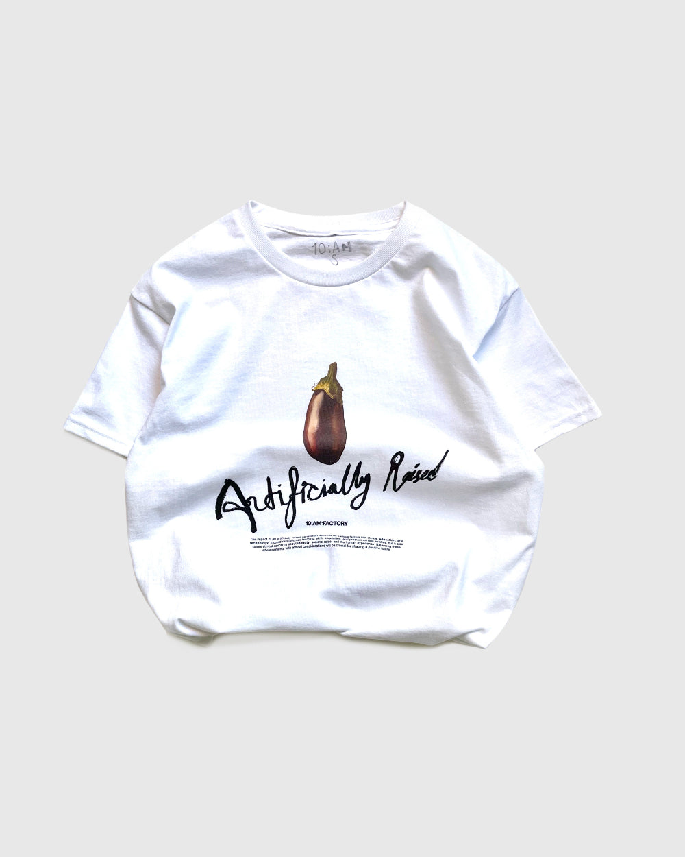 Unisex white 'Artificially Raised' t-shirt by 10:AM Factory, featuring a bold big eggplant graphic print and 10:AM logo, crafted from high-quality, soft cotton for a clean, modern look.