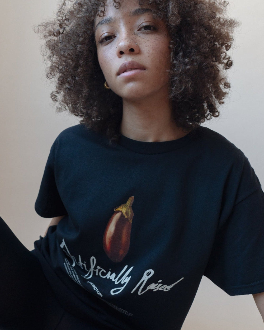 Unisex black 'Artificially Raised' t-shirt by 10:AM Factory, featuring a bold big eggplant graphic print and 10:AM logo, crafted from high-quality, soft cotton for a clean, modern look.